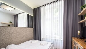 Una habitación de hotel moderna con una cama grande, un tocador de madera, un televisor y cortinas translúcidas.