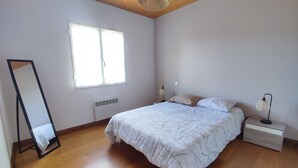 Un dormitorio con cama, mesita de noche, lámpara, espejo y ventana.