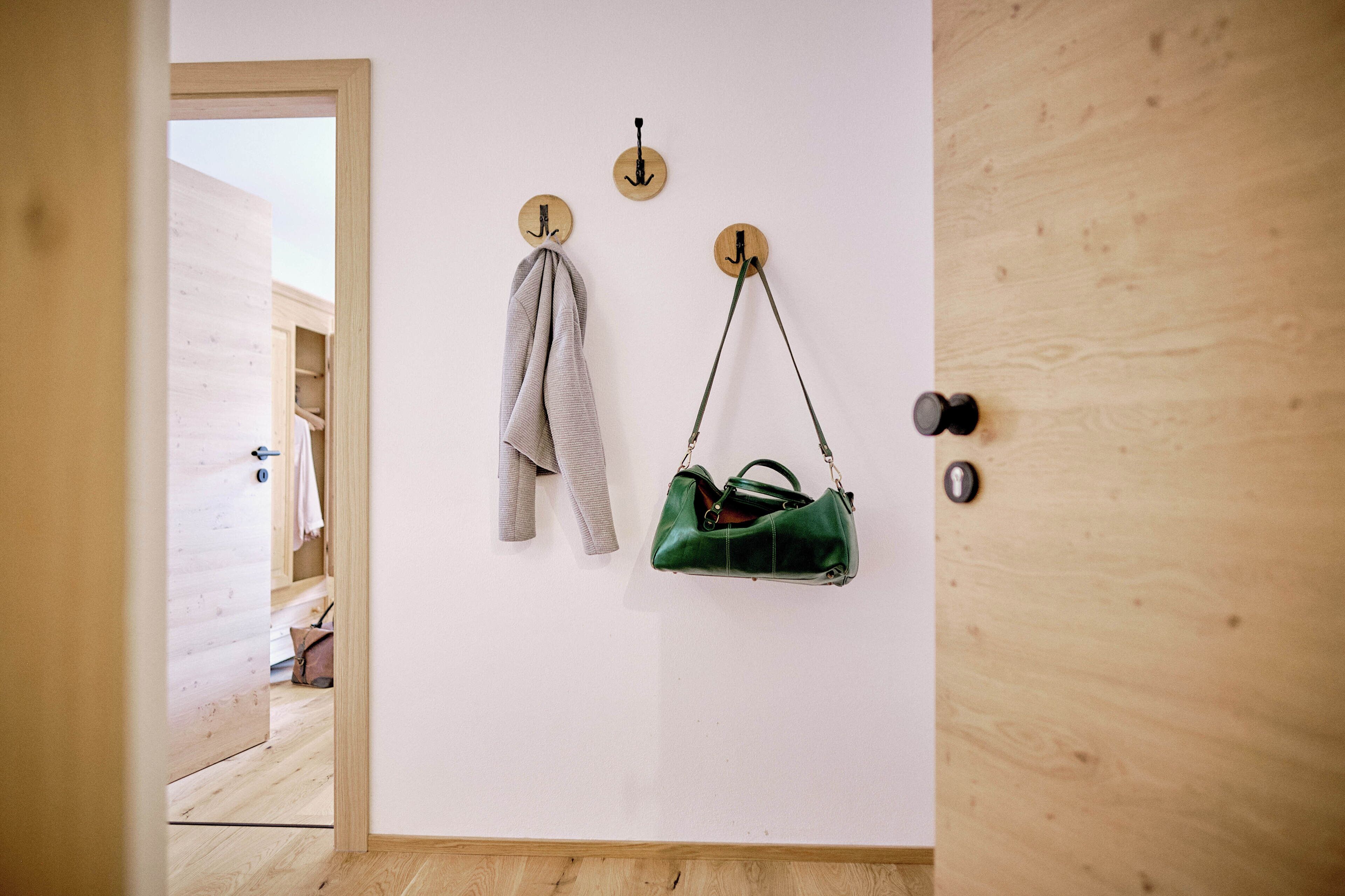 Un pasillo con una puerta de madera, un perchero con una chaqueta y un bolso verde colgado de un gancho.
