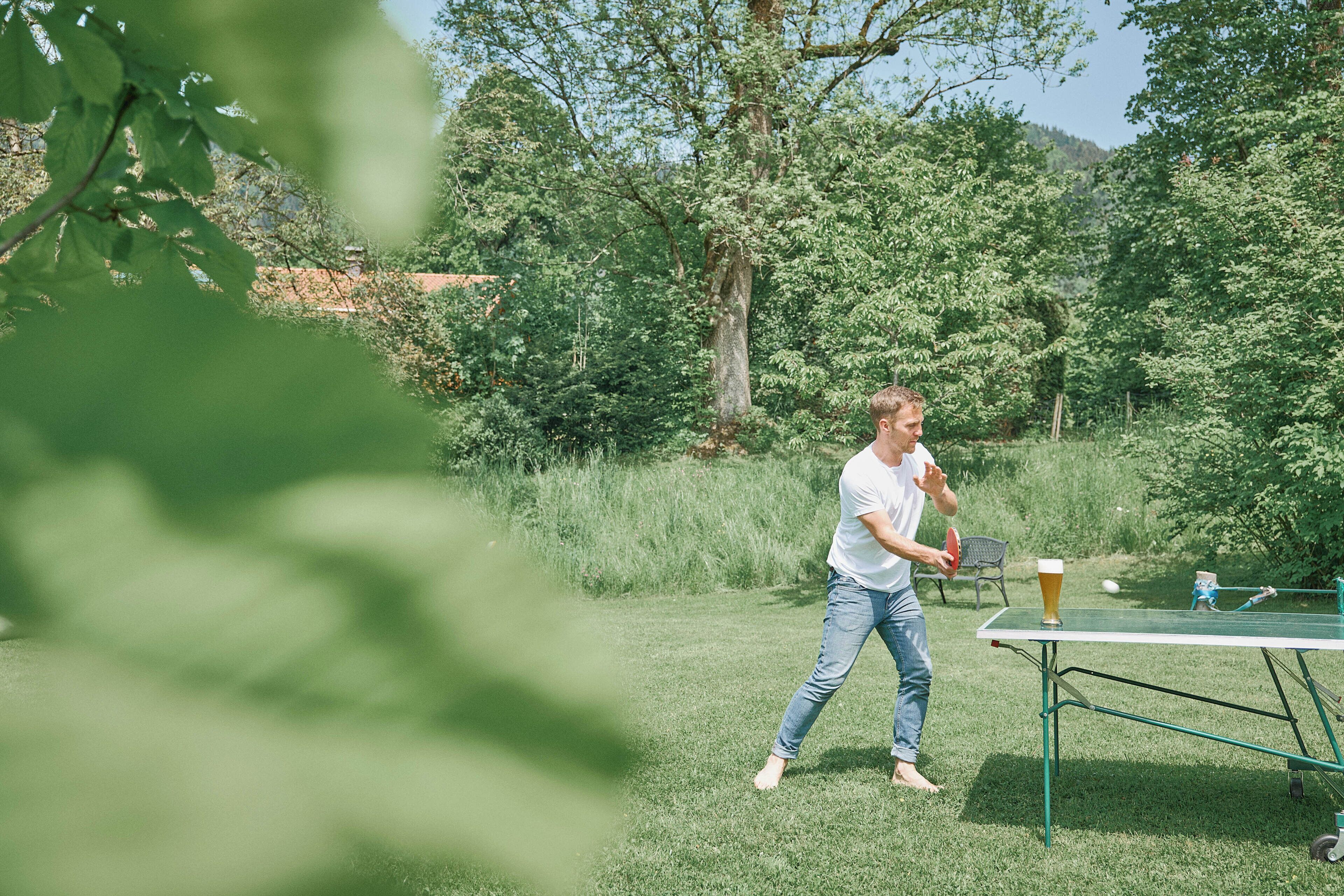 A person playing ping pong outdoors with a table and a glass of beer.