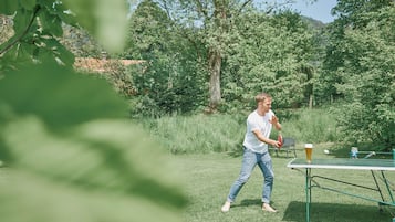 Une personne joue au ping-pong à l’extérieur, près d’une table, et a un verre de bière à portée de main.