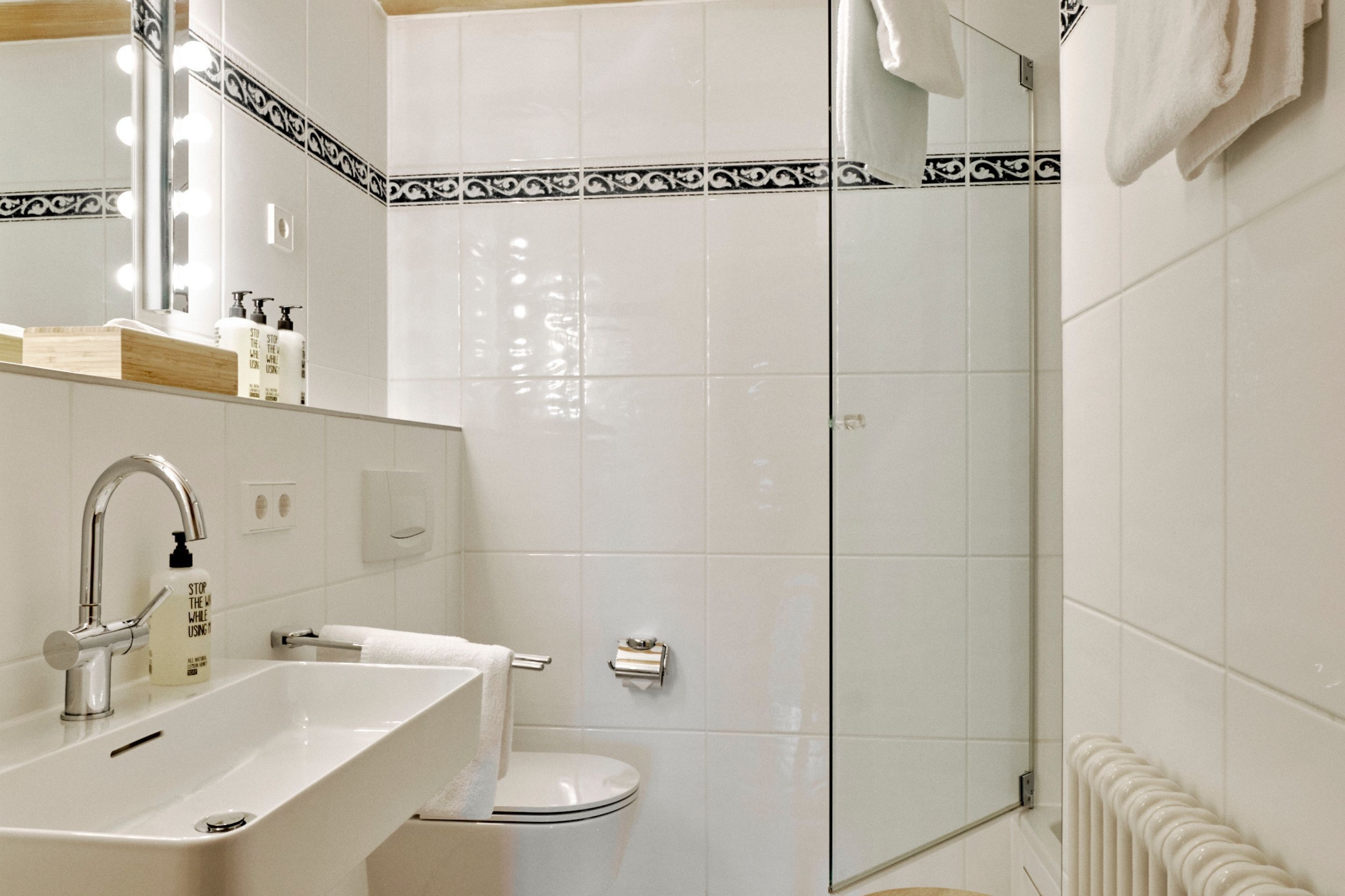 Un baño moderno con un lavamanos blanco, un espejo con iluminación, un inodoro y una cabina de ducha con mampara de vidrio.