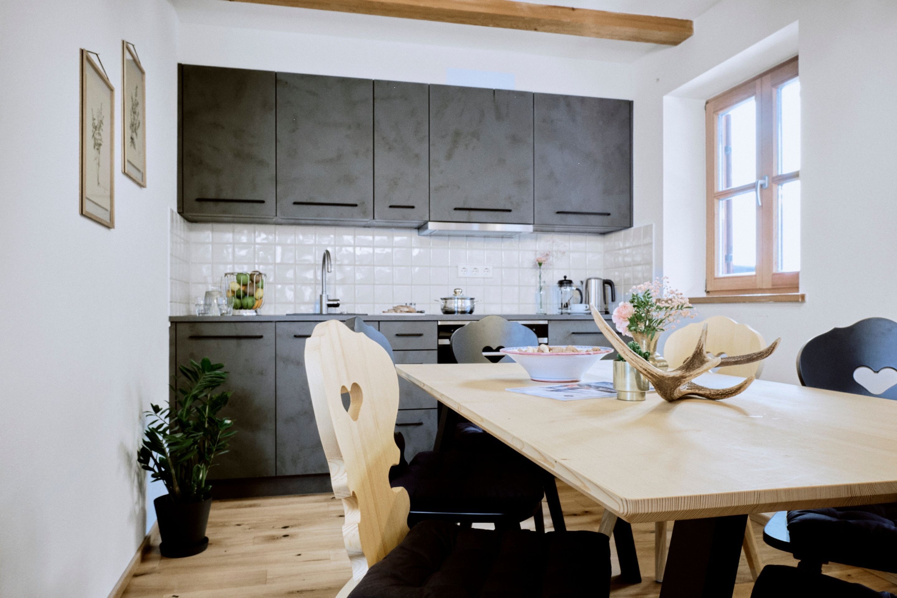 A modern kitchen with dark cabinets, a wooden dining table, and a potted plant.