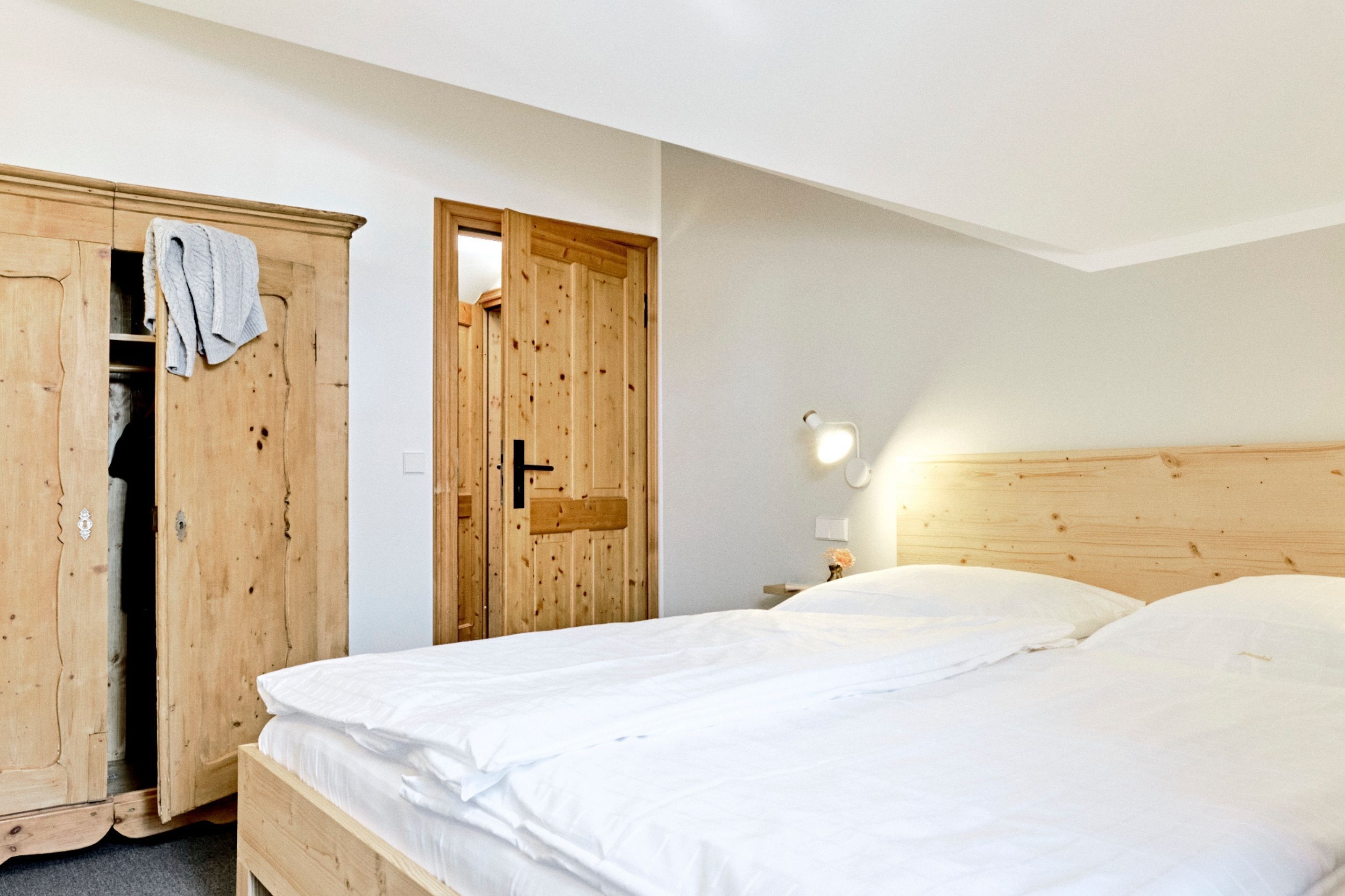 Een slaapkamer met een houten garderobe, een bed met witte beddengoed en een nachtkastje met een lamp.