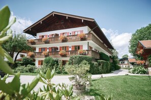 A multi-story building with balconies, surrounded by greenery and a clear sky. - Der Lederer Hof (Tegernsee)