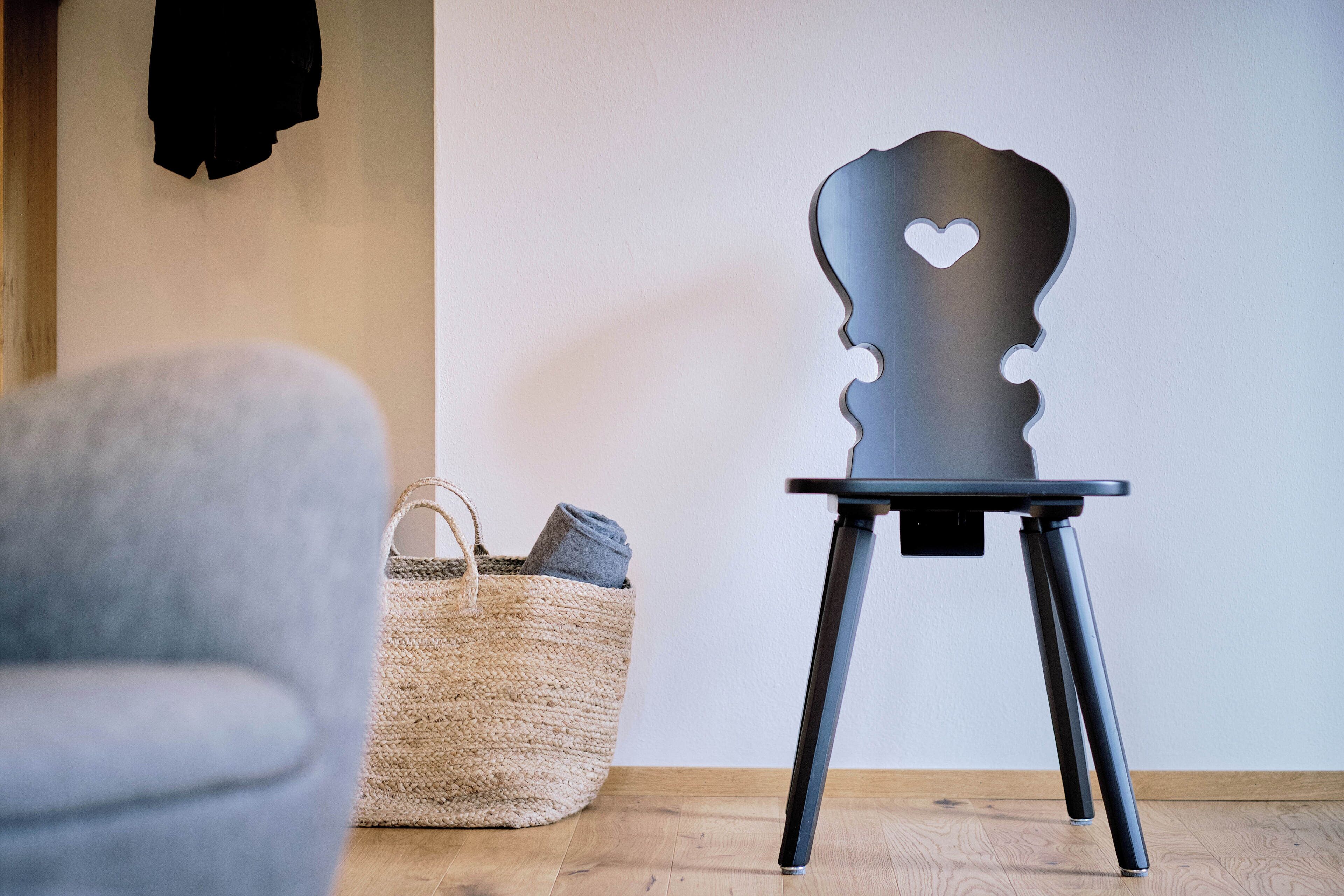 A room with a grey armchair, a woven basket, and a black chair with a heart-shaped cutout.