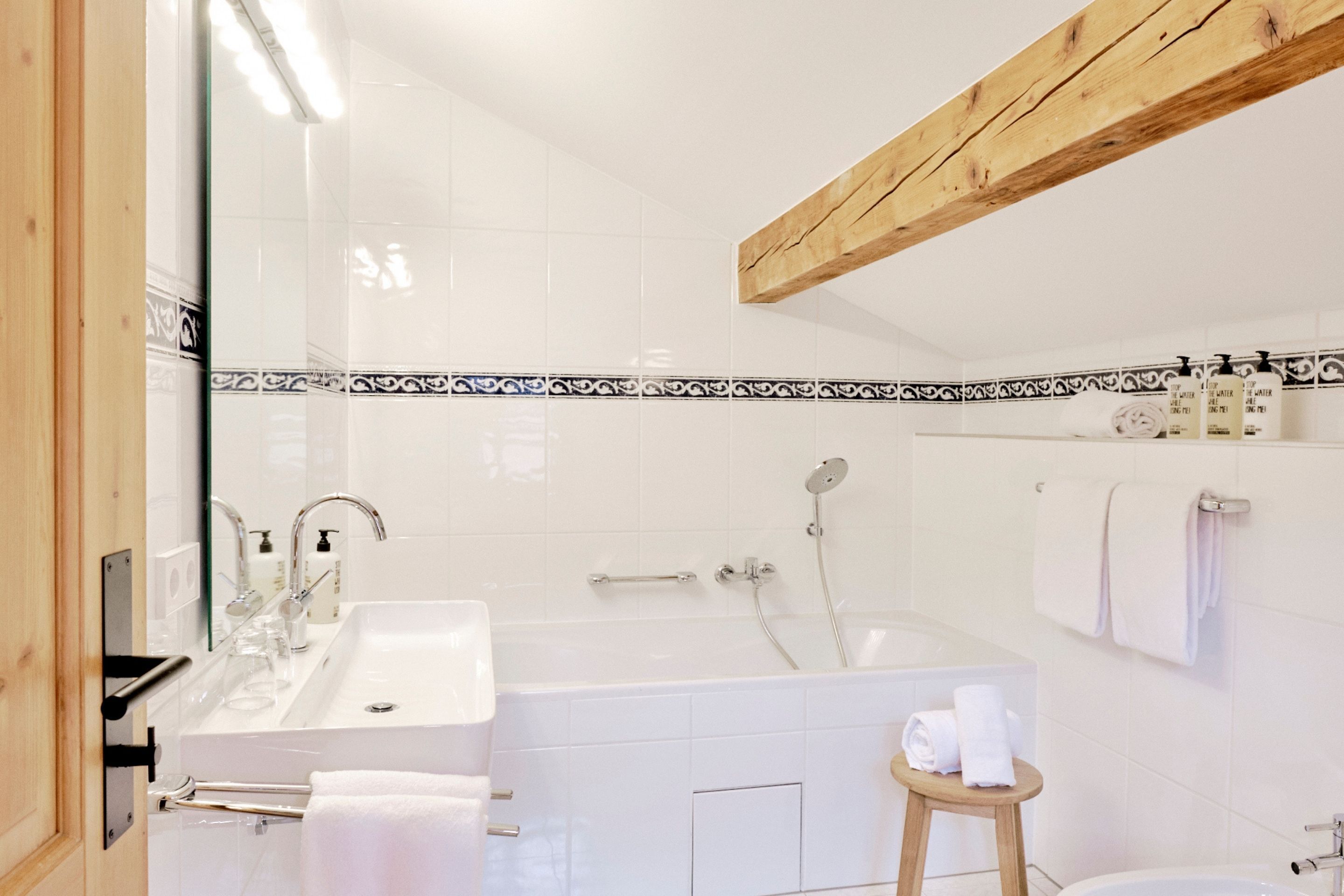 Ett modernt badrum med ett stort badkar, en handfat och en spegel. Handdukar och hygienartiklar finns på en hylla.