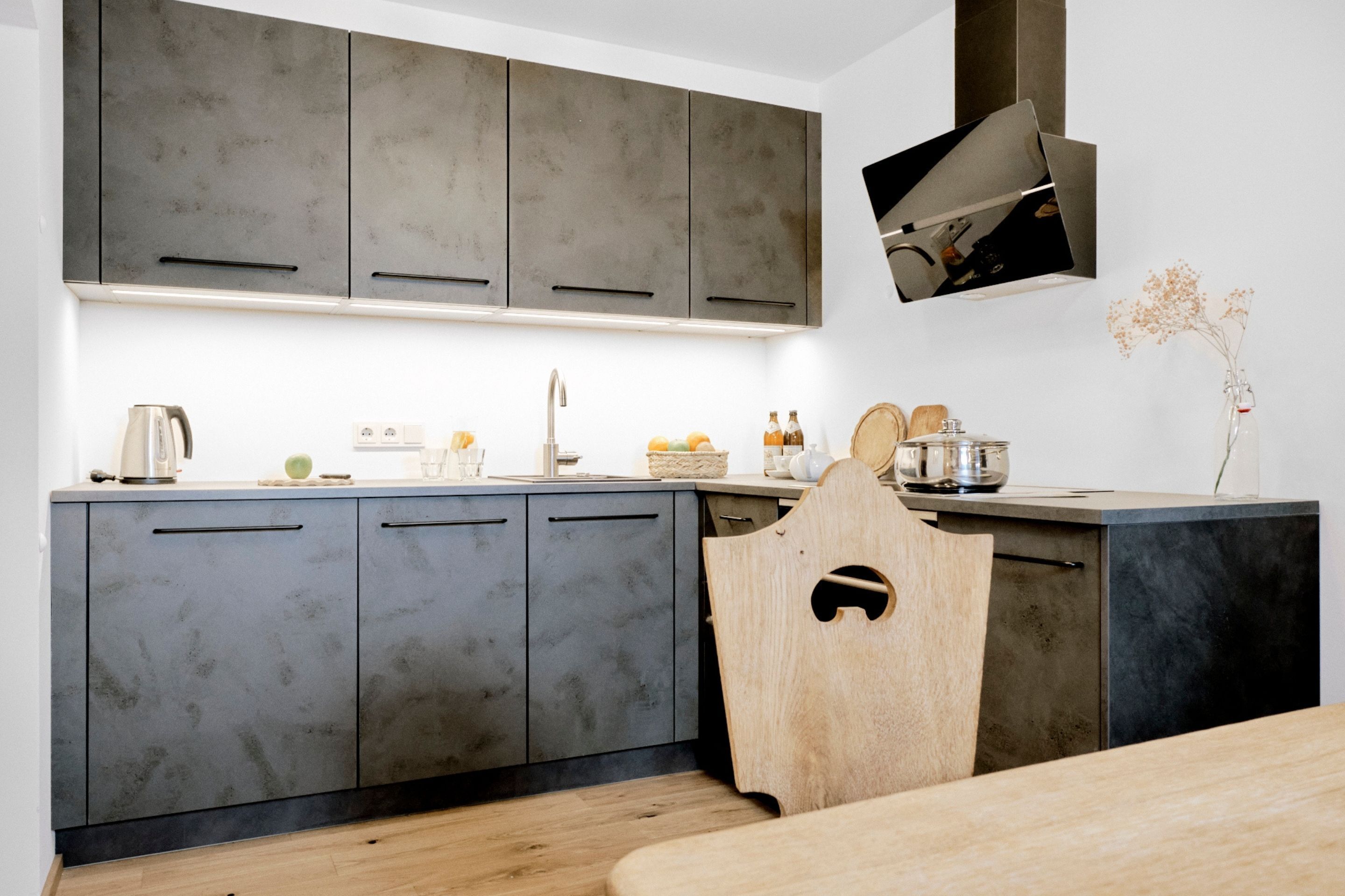 A modern kitchen with grey cabinets, a wooden chair, and a small table.