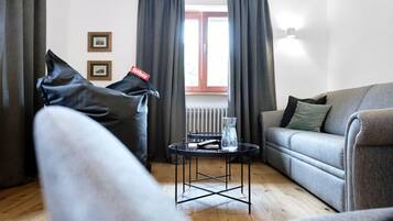 A modern living room with a grey sofa, a small round table with a vase, and a view of a window with curtains.
