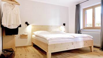 A wooden bed in a room with a hanging clothes rack, a bedside table, and a window with curtains.