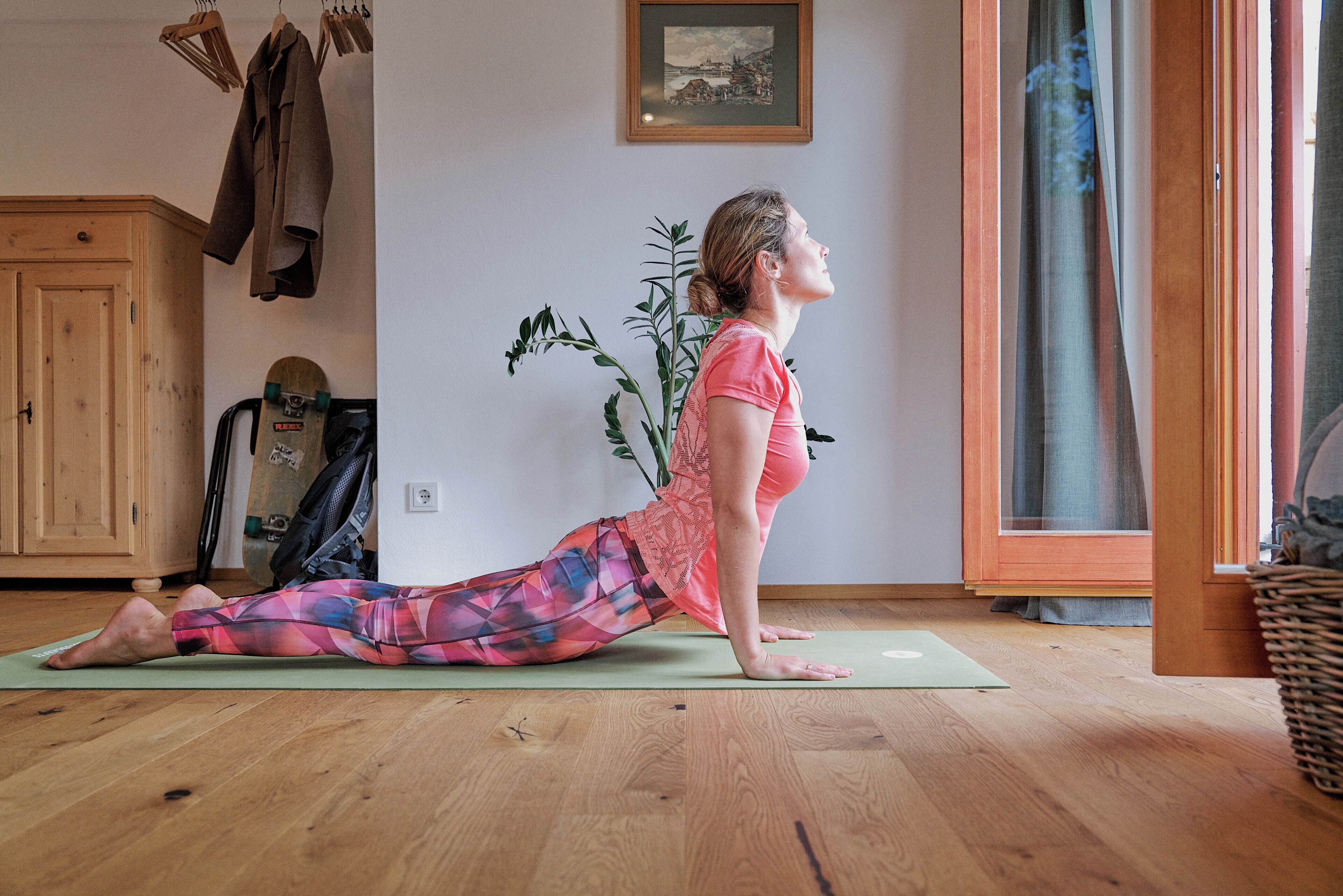 Un tapis de yoga sur un plancher en bois, avec une plante et un tableau encadré accroché au mur.