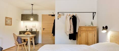 A bedroom with a bed, a wooden desk, a chair, a wardrobe, and a hanging clothes rack.