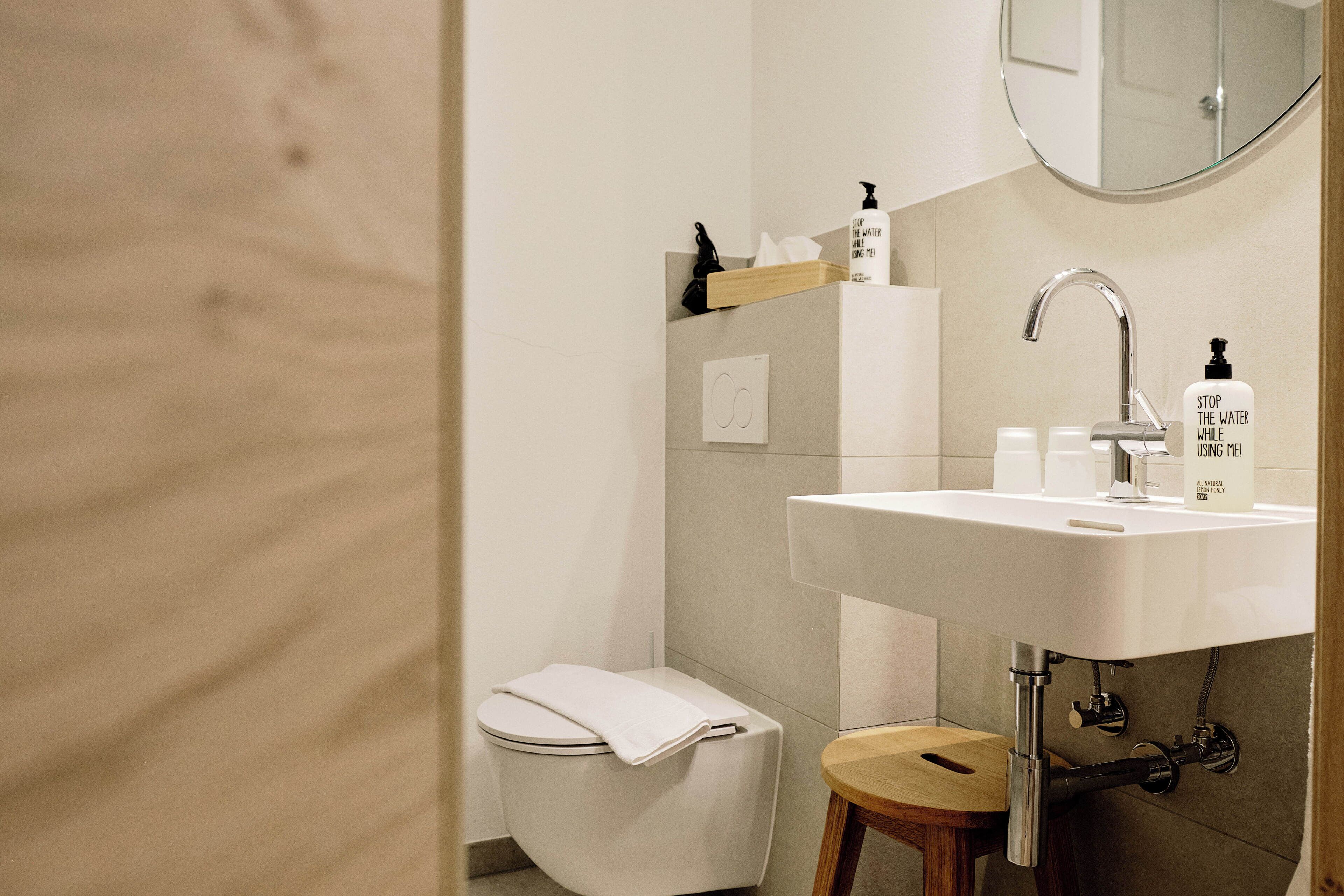Un baño moderno con un lavamanos blanco, un espejo encima y un inodoro con una toalla.