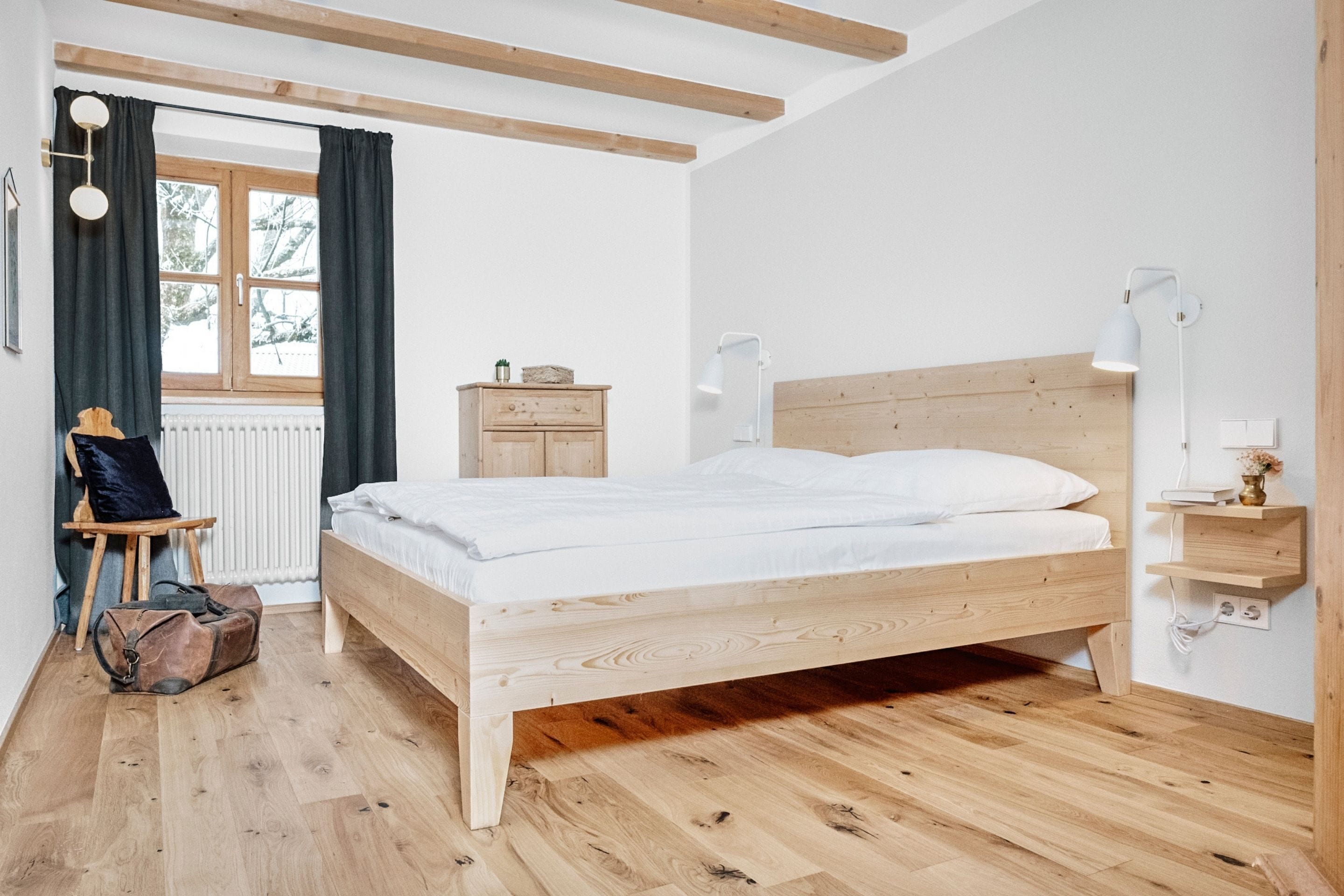 Een slaapkamer met een houten bed, een stoel, een bureau, een lamp en een raam met gordijnen.