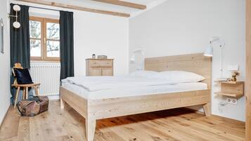 A bedroom with a wooden bed, a chair, a desk, a lamp, and a window with curtains.