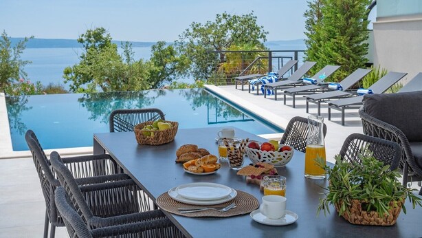 A dining table with breakfast items and a view of a pool and sea.