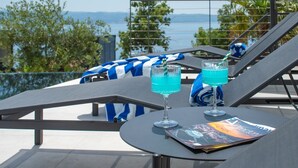 A poolside area with lounge chairs, a table with drinks, and a view of the sea.