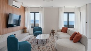 A modern living room with a sofa, a blue armchair, a coffee table, and a TV mounted on the wall.