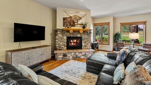 A living room with a stone fireplace, leather sofas, a flat-screen TV, and a large window. - Relax and Recharge at The Retreat at The Enclave – Mountain Views, Hot Tub, and (Steamboat Springs)