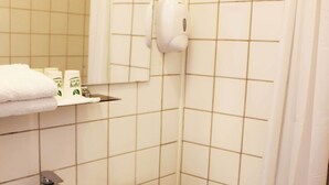 Une salle de bain avec un lavabo blanc, des toilettes et un miroir au-dessus du lavabo. On y trouve une étagère avec des articles de toilette et un rideau de douche.