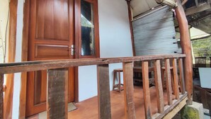 Eine Holztür mit Glasfenster, einem Metallrollgitter und einem kleinen Hocker auf einer Veranda.