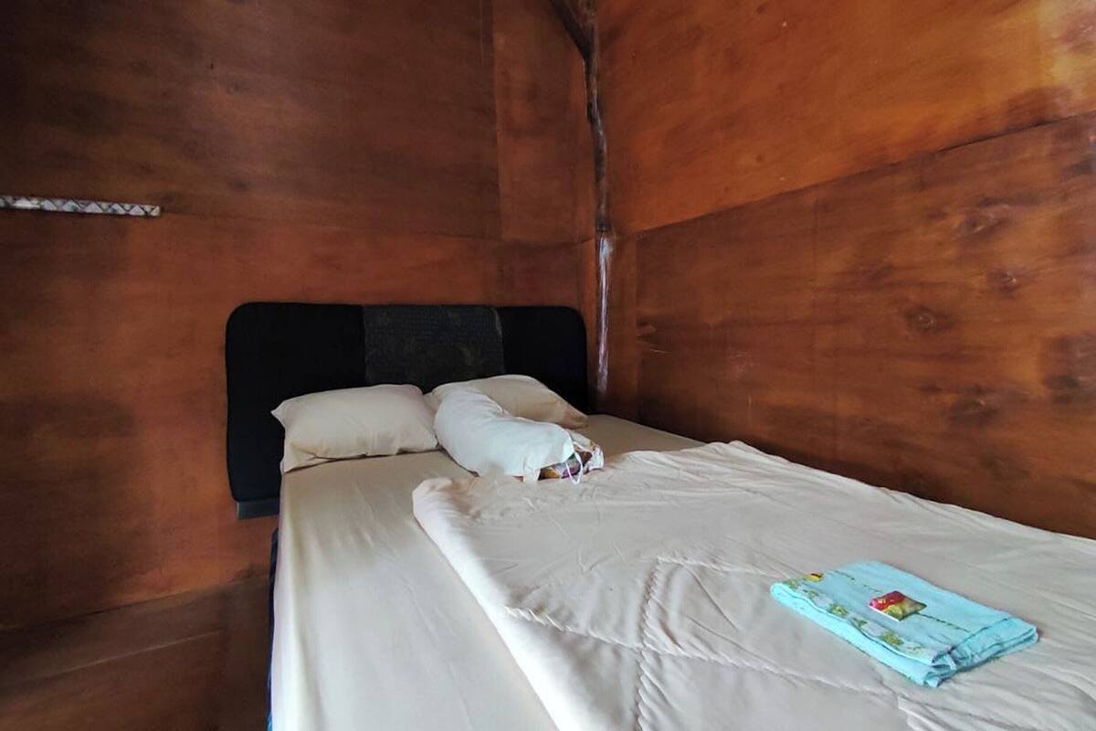 Ein Einzelbett mit weißer Matratze und Kissen, eine zusammengefaltete blaue Decke und ein Holz-Kopfstück.