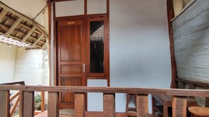 Eine Holztür mit kleinem Fenster, einem geschlossenen Metallrollladen und einem Holzgeländer.