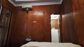 Ein Zimmer mit Holzwänden, einem Bett, einem kleinen Tisch mit Lampe und einer Klimaanlage an der Wand.