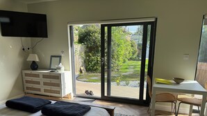 Un dormitorio con cama, escritorio, silla, televisor y vista a un jardín a través de una puerta corrediza.