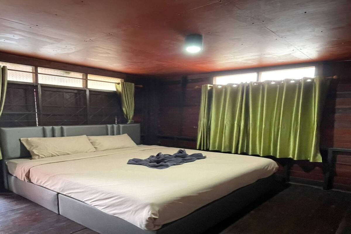 Habitació amb un llit gran, parets de fusta i cortines verdes.