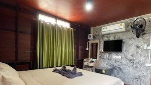 Une chambre à coucher comprenant un lit, un bureau, un climatiseur, une télévision et une fenêtre avec des rideaux.