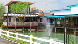 Un restaurant situé au bord de l’eau, doté d’une terrasse, d’un élément décoratif aquatique et d’une clôture blanche.