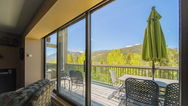 Un balcon avec vue sur les montagnes, un parasol vert et du mobilier d’extérieur.