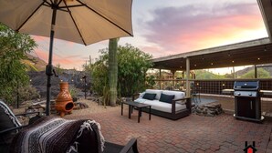 En udendørs terrasse med sofa, bord, grill og parasol.