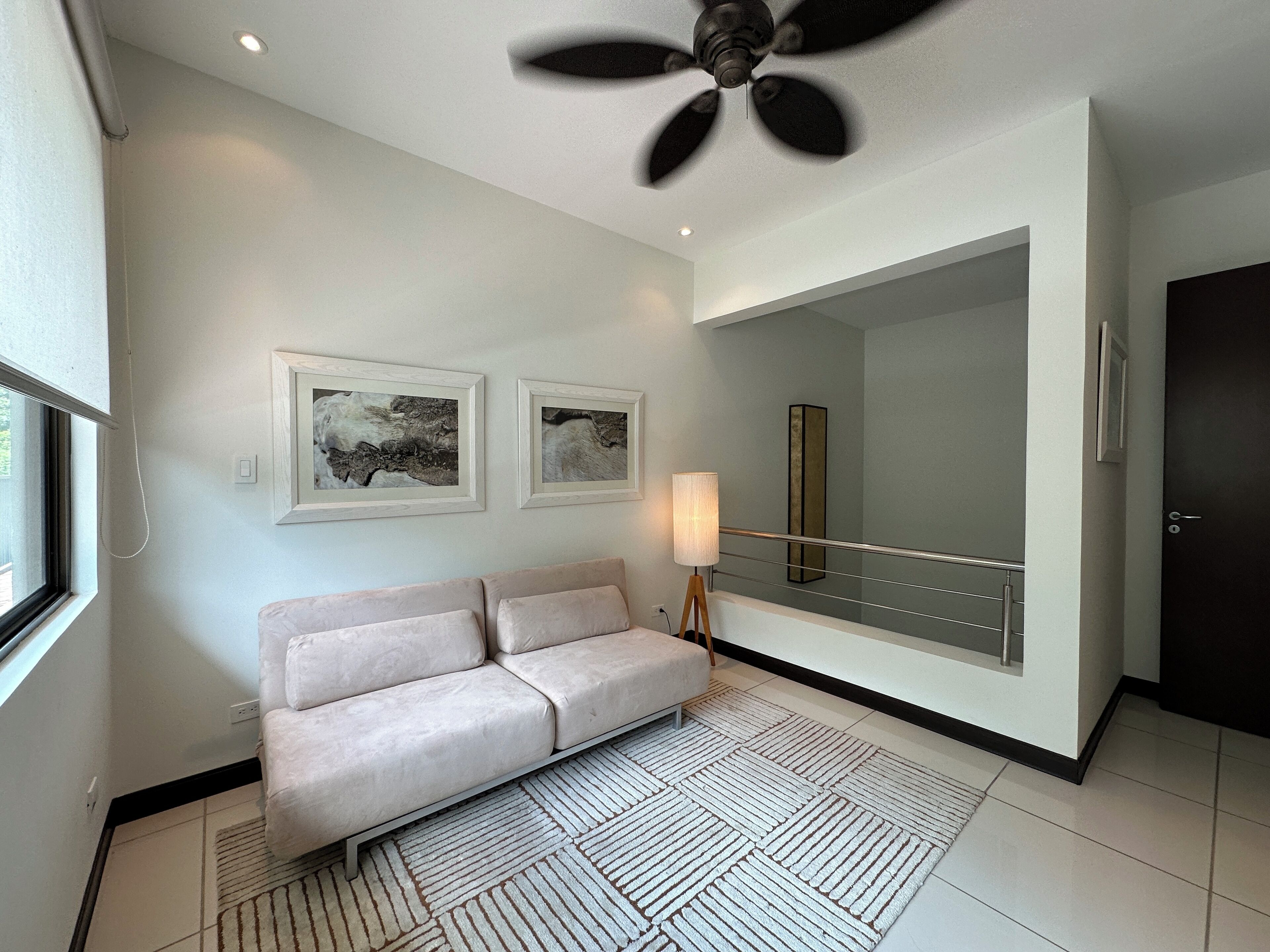 A modern hotel room with a beige sofa, a large mirror, and two framed artworks on the wall.