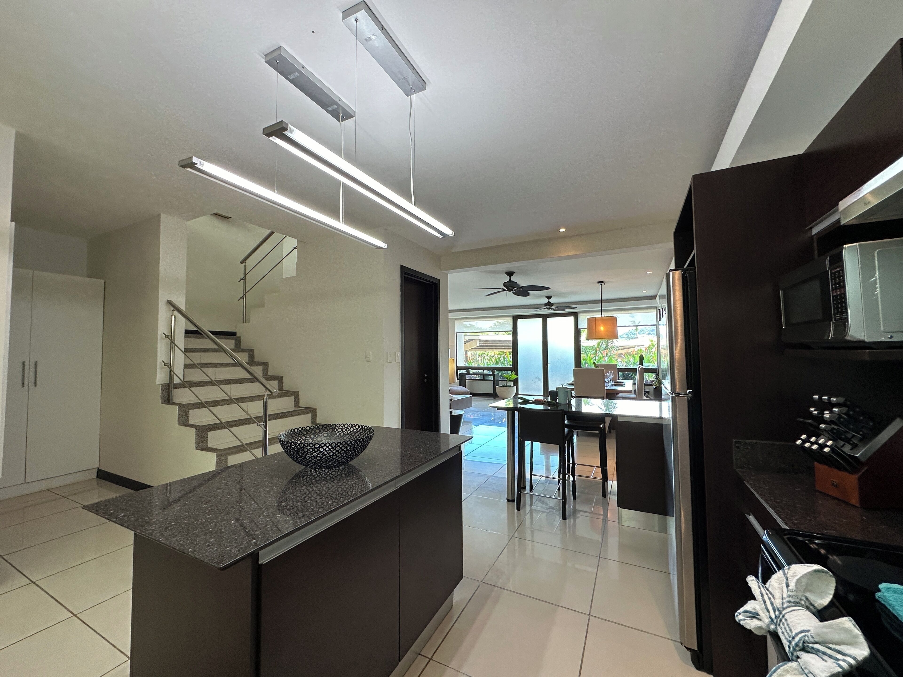 Una cocina moderna con una isla central, electrodomésticos integrados y una escalera que sube a otro nivel.