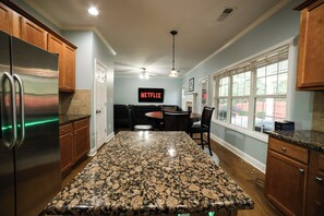 A kitchen with granite countertops, wooden cabinets, a stainless steel refrigerator, and a wall-mounted TV displaying 'NETFLIX'.
