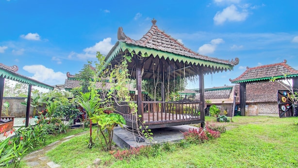A traditional pavilion with a tiled roof, surrounded by lush greenery and a stone pathway. - Capital O 94018 Joglo Eyang Niek Turi Syariah (Kaliurang)