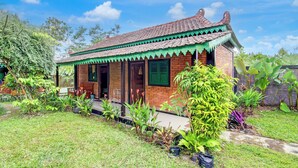 A traditional house with a tiled roof, brick walls, and a porch with green shutters. - Capital O 94018 Joglo Eyang Niek Turi Syariah (Kaliurang)
