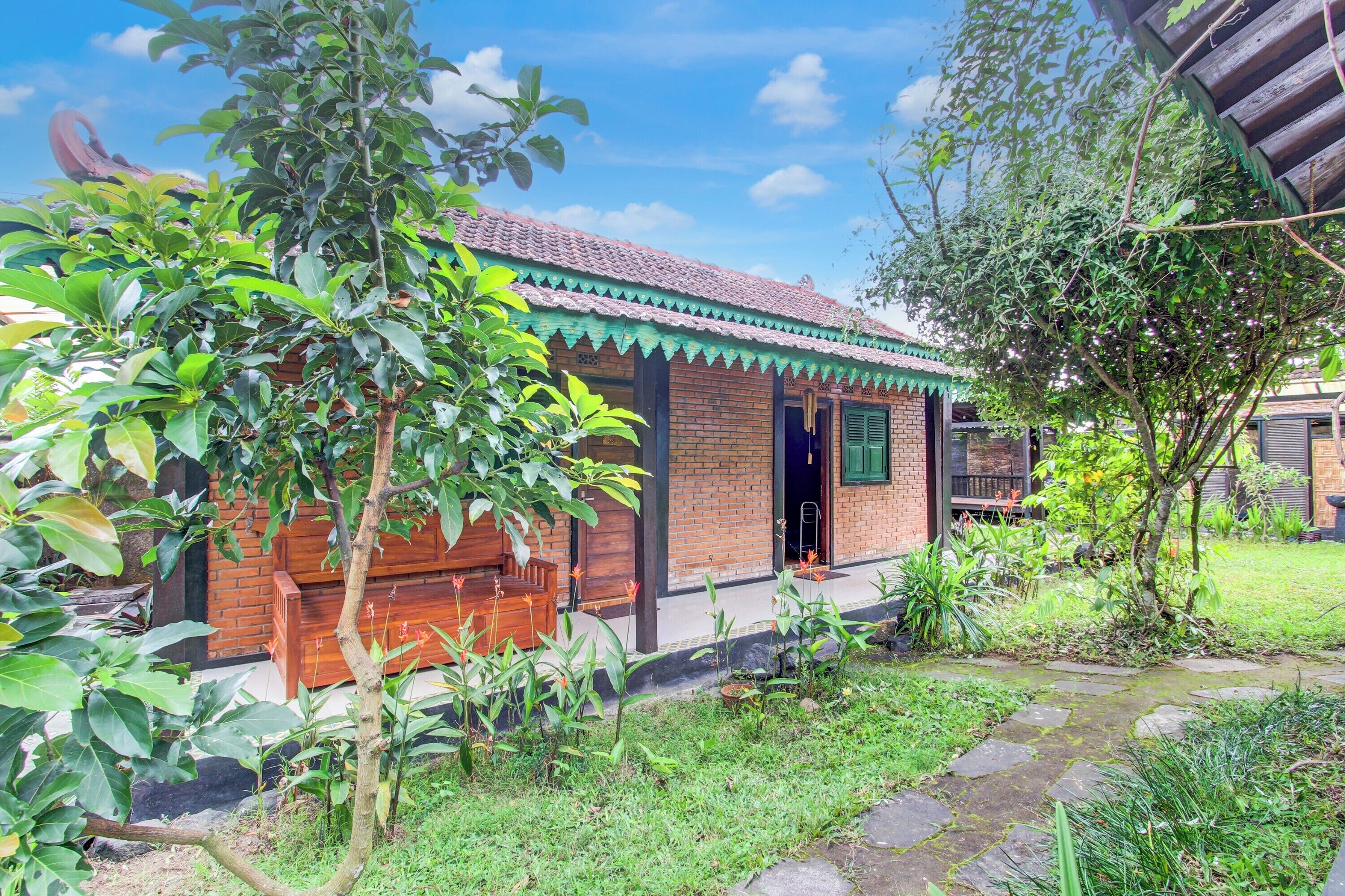A traditional brick house with a tiled roof, surrounded by lush greenery and a stone pathway.