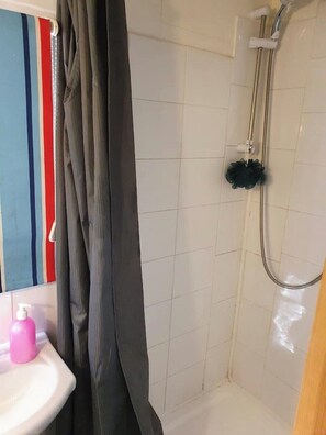Ein Badezimmer mit Dusche, Waschbecken und Spiegel, mit einem gestreiften Handtuch an der Wand.