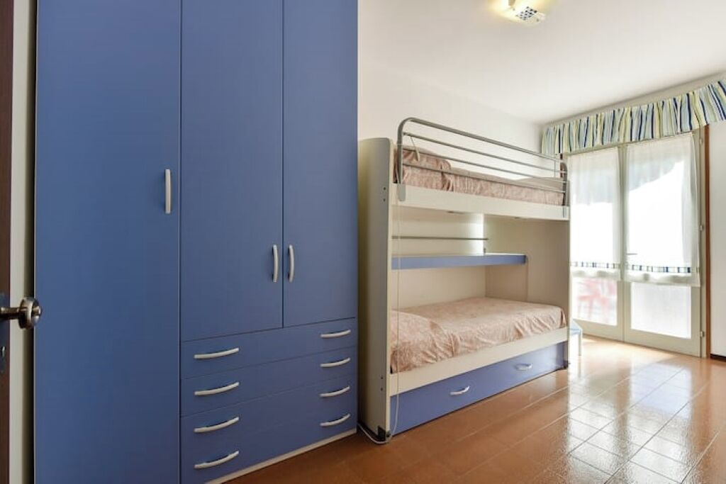 A bedroom with a bunk bed, a blue wardrobe, and a sliding glass door to a balcony.