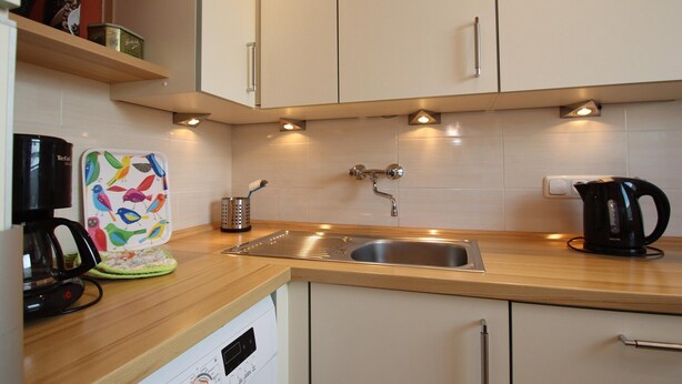 A modern kitchen with a stainless steel sink, wooden countertop, and white cabinets. - Bungalow in Dornumersiel (Dornumersiel)