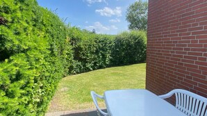 A patio with a white table and chairs, a brick wall, and a well-maintained hedge. - Bungalow in Dornumersiel (Dornumersiel)