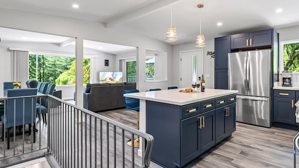 A modern kitchen with dark cabinets, a stainless steel refrigerator, and a dining area with blue chairs.