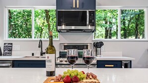 A kitchen with a wine bottle, two glasses of red wine, and a charcuterie board with grapes, strawberries, and cheese.