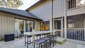 Un patio extérieur couvert, avec une longue table et plusieurs tabourets de bar, une petite poubelle et une terrasse en bois.