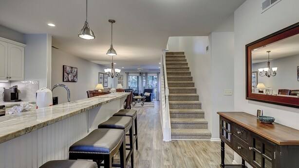 Une cuisine moderne dotée d’un plan de travail en marbre, de tabourets de bar, de luminaires suspendus et d’un escalier menant à un espace de vie offrant une vue sur l’extérieur.