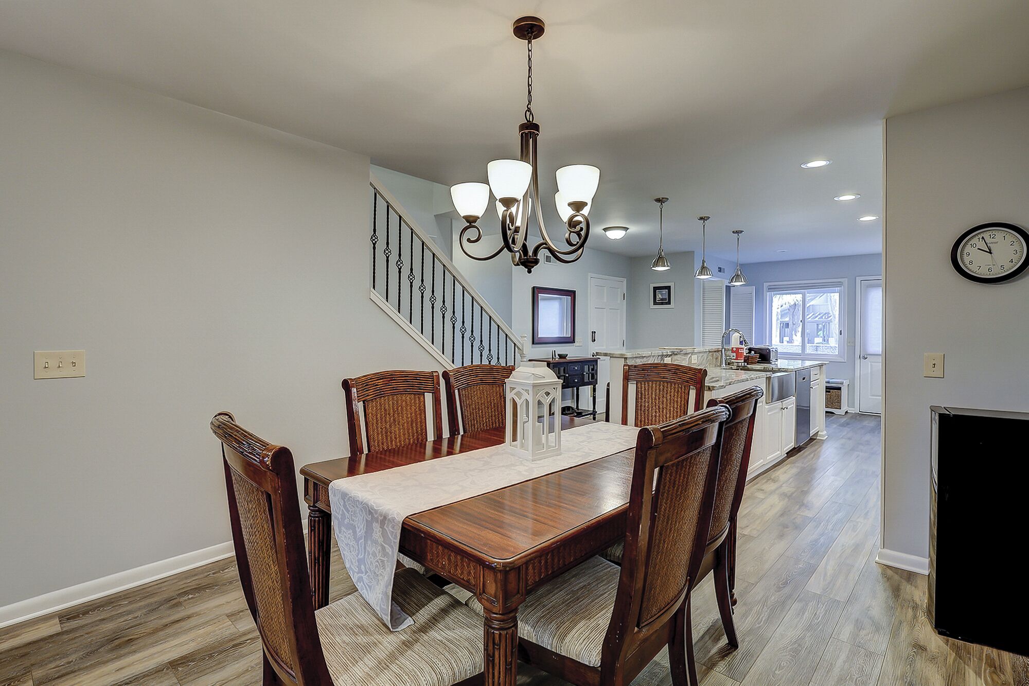 A spacious dining area with a wooden table and chairs, a chandelier, and a staircase leading to another level.