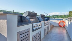 Un espace cuisine extérieur équipé d’un barbecue, d’une bouée de sauvetage et offrant une vue sur une piscine et des collines en arrière-plan.